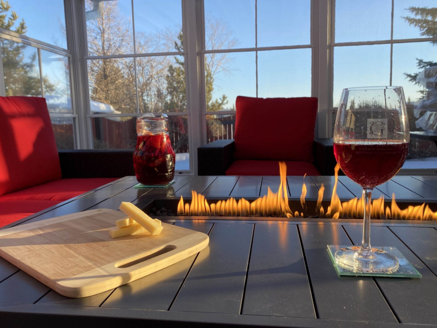 Sunlit lounge with fire table, red chairs, wine glasses, and a cutting board on the table