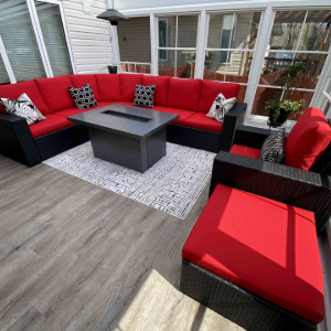 Red outdoor patio sectional with black cushions, gray fire pit table, and bright red ottoman on a deck