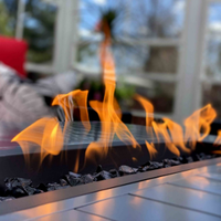 Outdoor gas fire pit with bright orange flames on a tiled patio, blurred house in the background