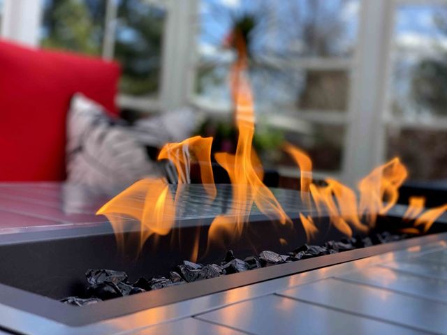 Modern fire pit with orange flames on a tiled patio beside a red chair
