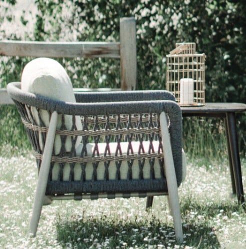 Wicker chair beside a wooden table with a birdcage in a grassy garden setting