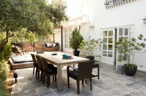 Courtyard patio with wooden dining table, chairs, potted plants, and glass doors on a white building