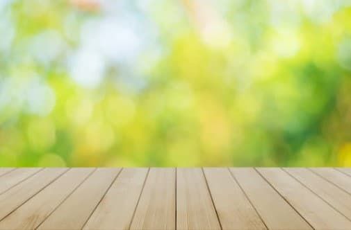 Wooden tabletop in front of a blurred green and yellow garden background