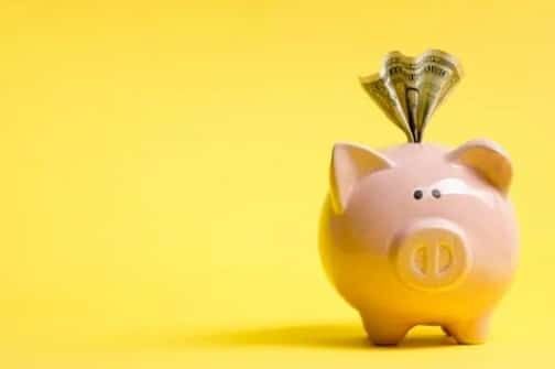 Pink piggy bank with folded dollar bills on a bright yellow background