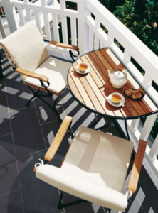 Small balcony with two cream chairs and a round table set with tea and pastries in sunlight.
