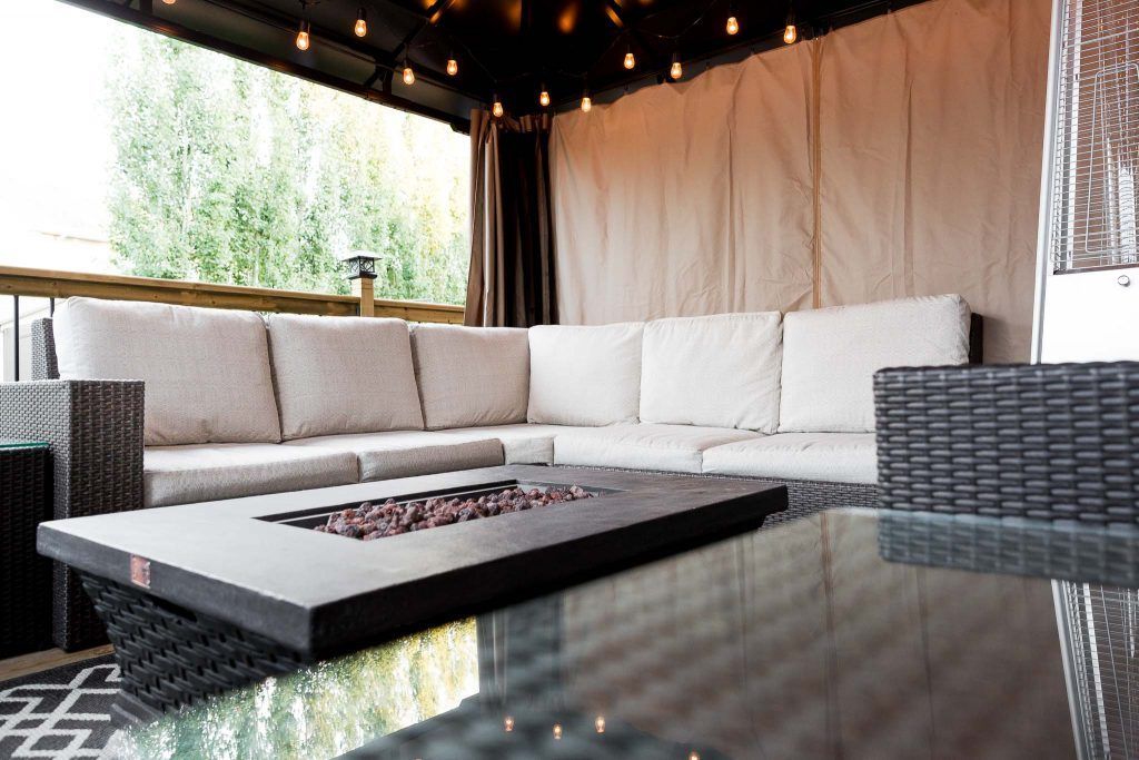 Modern patio lounge with white sectional seating, glass fire pit, and string lights under a canopy