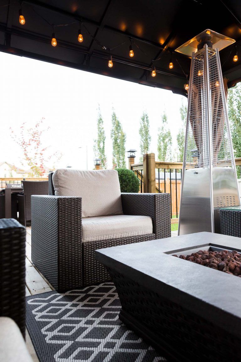 Modern patio seating with wicker chairs, string lights, and a tall fire pit under a covered pergola