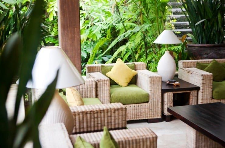 Tropical patio seating with wicker chairs, green cushions, and white lamps amid lush plants