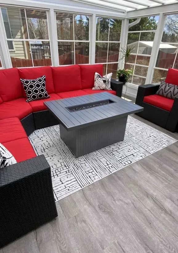 Red and black sectional patio sofa around a gray coffee table in a bright sunroom with large windows.