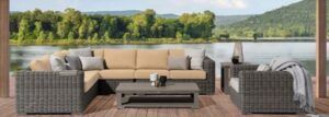 Outdoor wicker patio seating with beige cushions, coffee table, and lake view at sunset