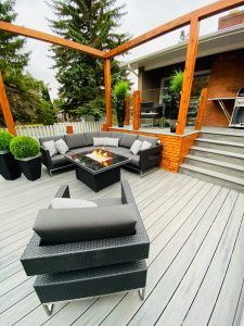 Modern outdoor patio with gray sectional seating, fire pit, and wooden pergola beside a house
