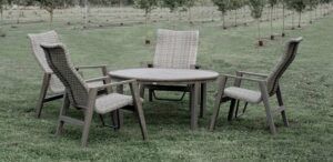 Outdoor patio set with four wicker chairs around a round table on grass, with trees in the background