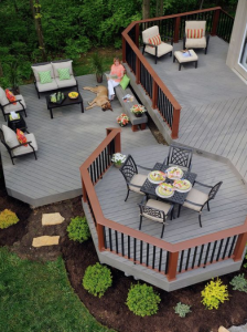 Tiered wooden deck with black patio furniture, potted plants, and two people relaxing outdoors