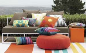 Outdoor patio seating with colorful pillows, orange pouf, and striped rug overlooking a landscape