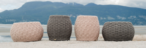 Four woven pouf stools in beige, gray, and pink sit outdoors before mountains.