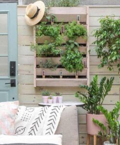 Patio wall with hanging plants, straw hat, and a small couch with patterned pillows and potted greenery
