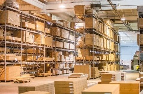 Warehouse aisles lined with tall pallet racks and stacked cardboard boxes under bright industrial lighting