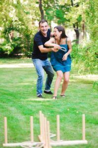 Two people carrying a wooden object through a grassy park, with a wooden frame in the foreground.