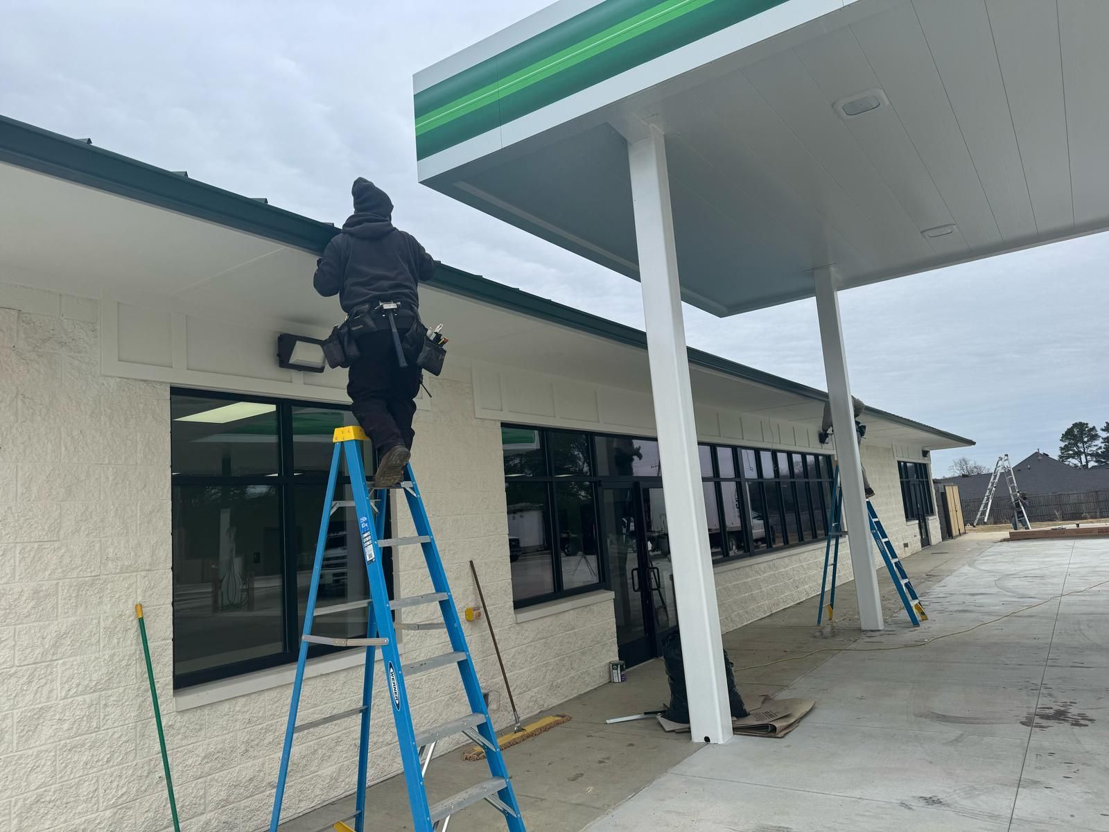Person cleaning windows on a ladder at a BP gas station with a white and green canopy.