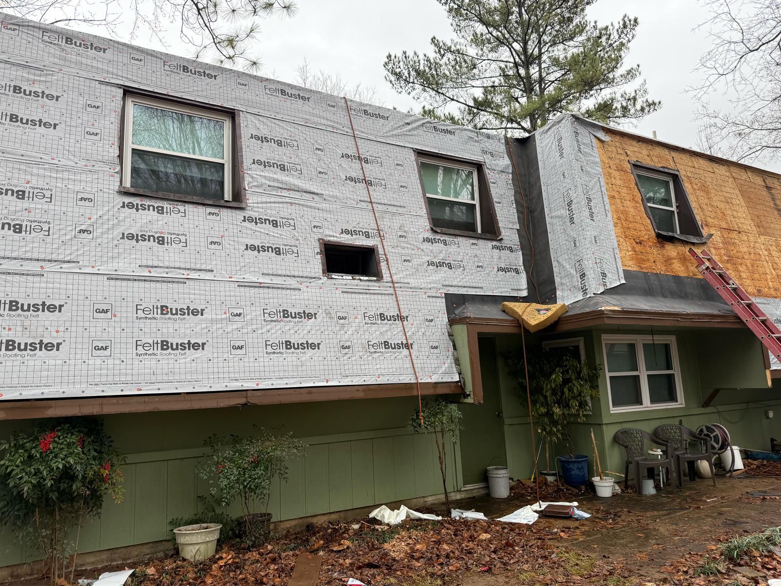 House under construction: roofing and siding partially removed. Green exterior, gray underlayment.