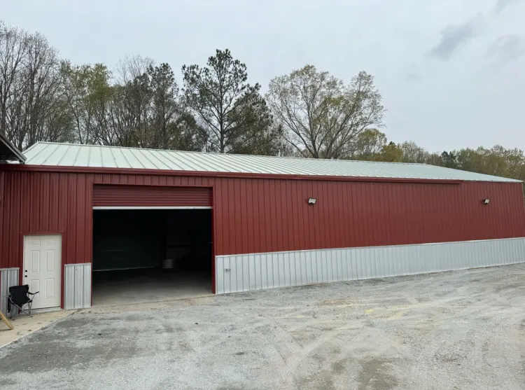 Red and silver metal building with an open garage door and a white door, set in a gravel lot.