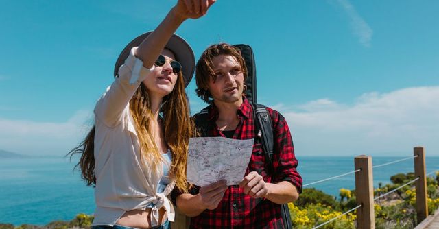Dos excursionistas estudian un mapa en un mirador costero soleado con el océano de fondo.