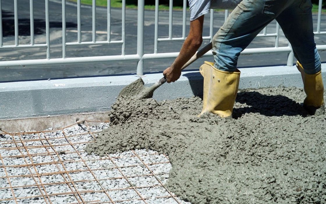 A man is spreading concrete on the ground with a shovel.