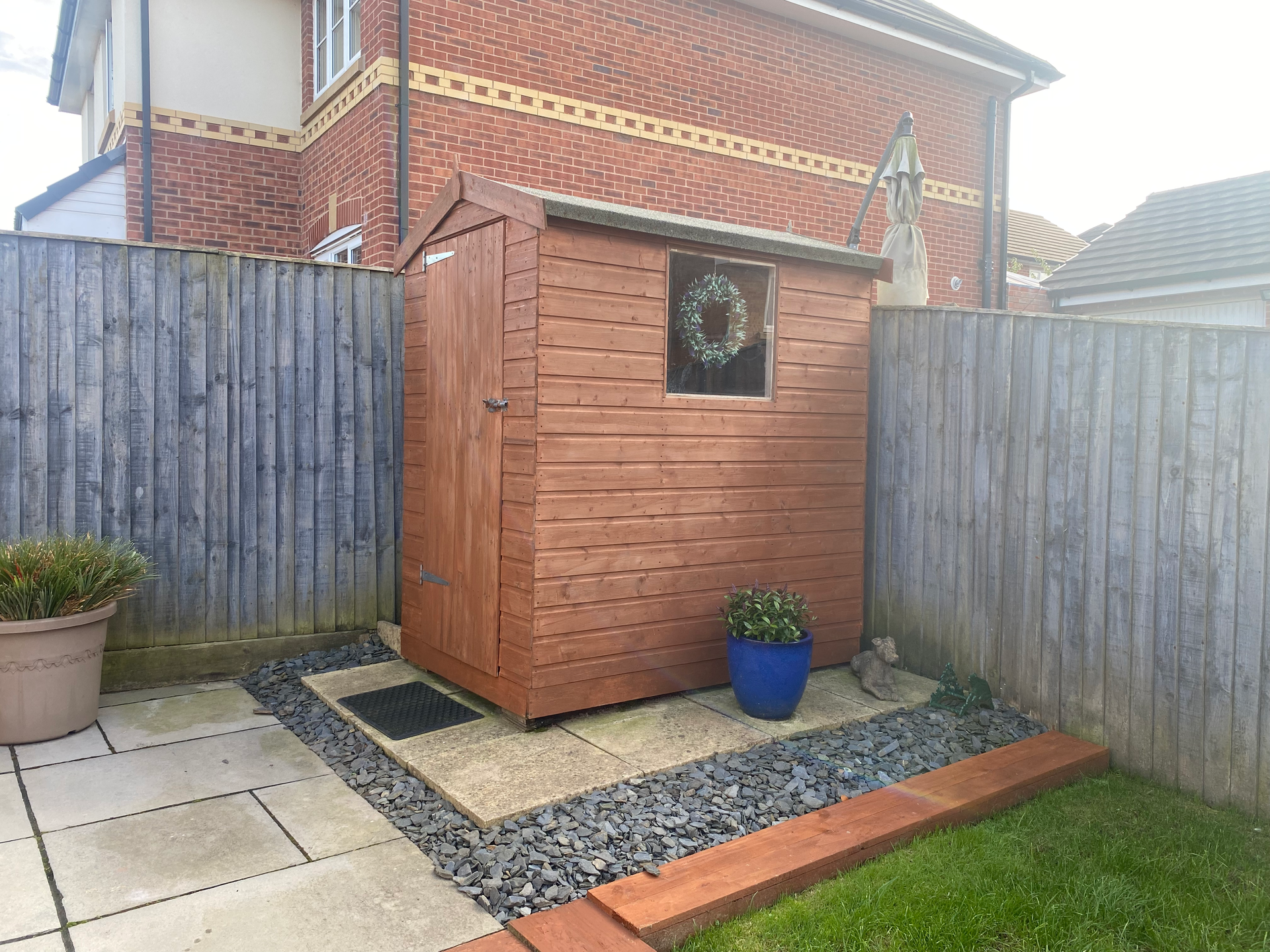 shed and sleepers in a garden setting, stained in a rustic orange/red colour.
