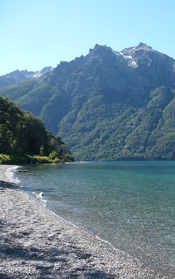 Un lago con montañas al fondo y una playa en primer plano.