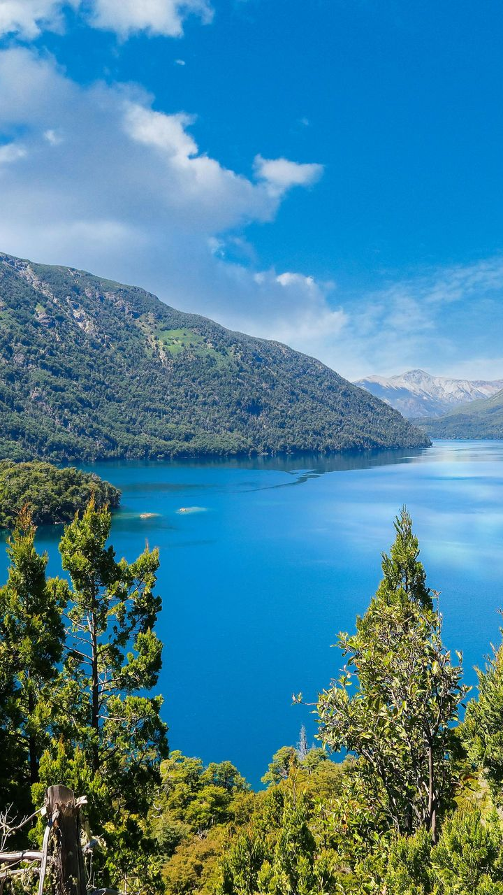 Un lago con montañas al fondo y una playa en primer plano.