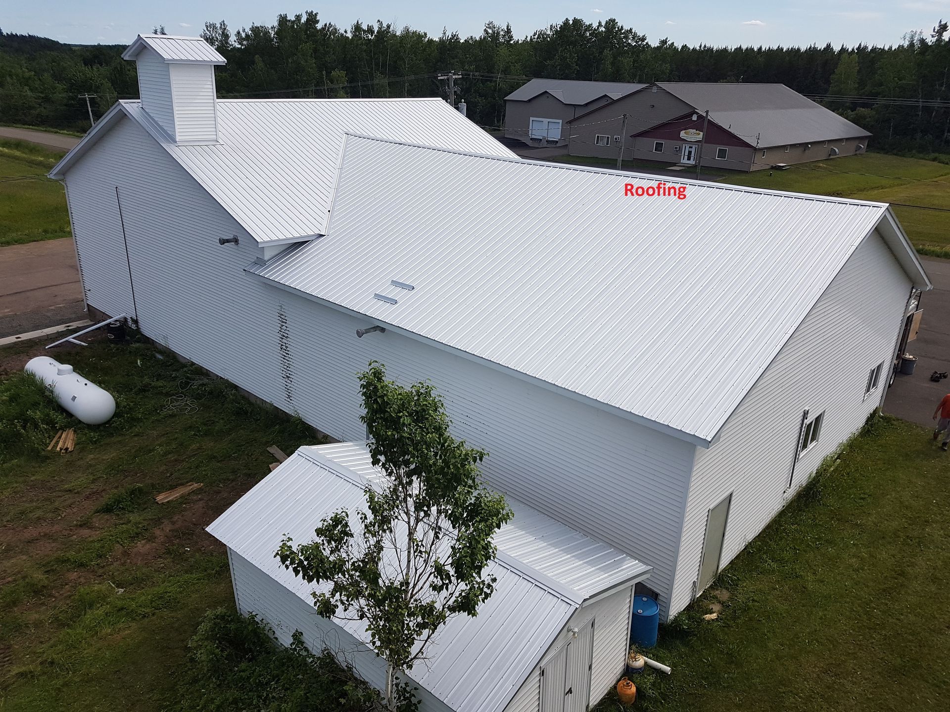 An aerial view of a white barn with a roof that has been painted white.