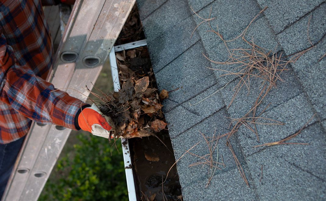 A man is cleaning a gutter on a roof with a shovel.
