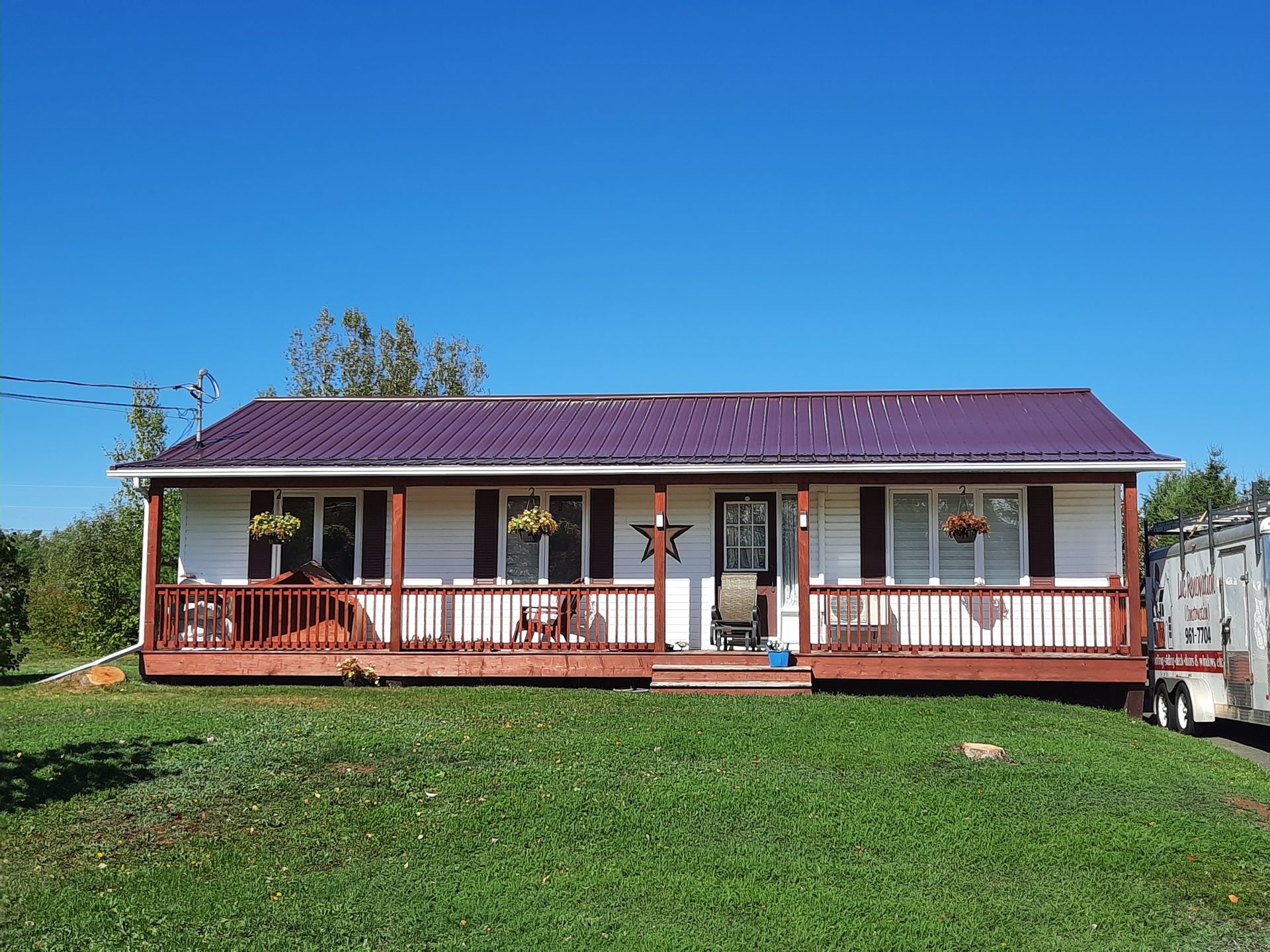 A house with a purple roof and a porch is sitting on top of a lush green field.