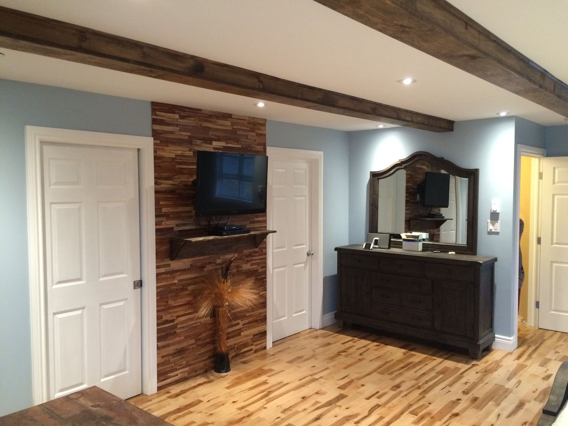 Living room with wood ceiling beams, brick accent wall, TV, and dark dresser with mirror