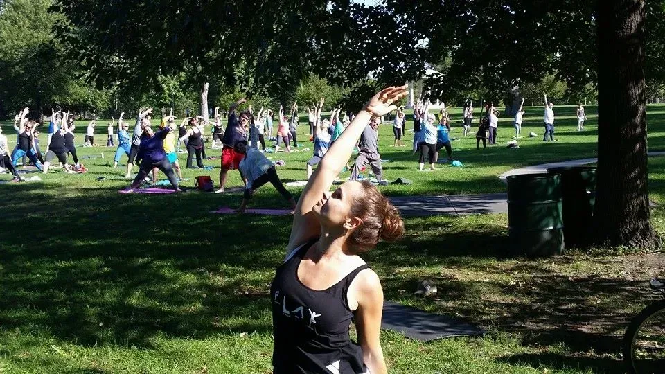 A woman is standing in front of a group of people doing yoga in a park.