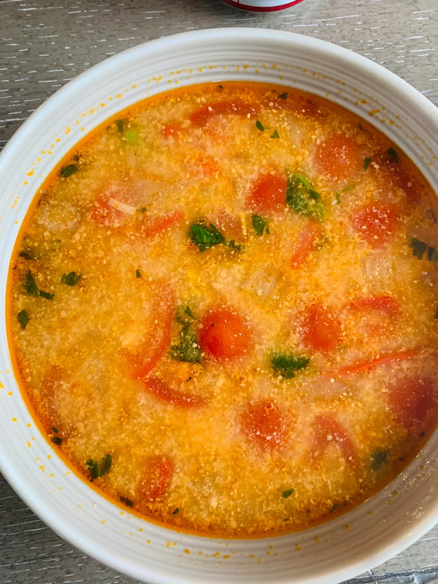 A bowl of soup with tomatoes and broccoli on a table.