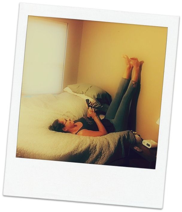A woman is laying on a bed with her legs up on the wall