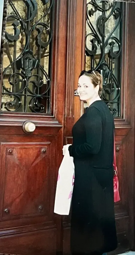 A woman in a black coat is standing in front of a wooden door.