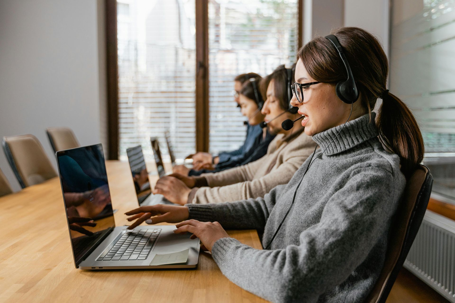 A group of people wearing headsets are sitting at a table using laptops.