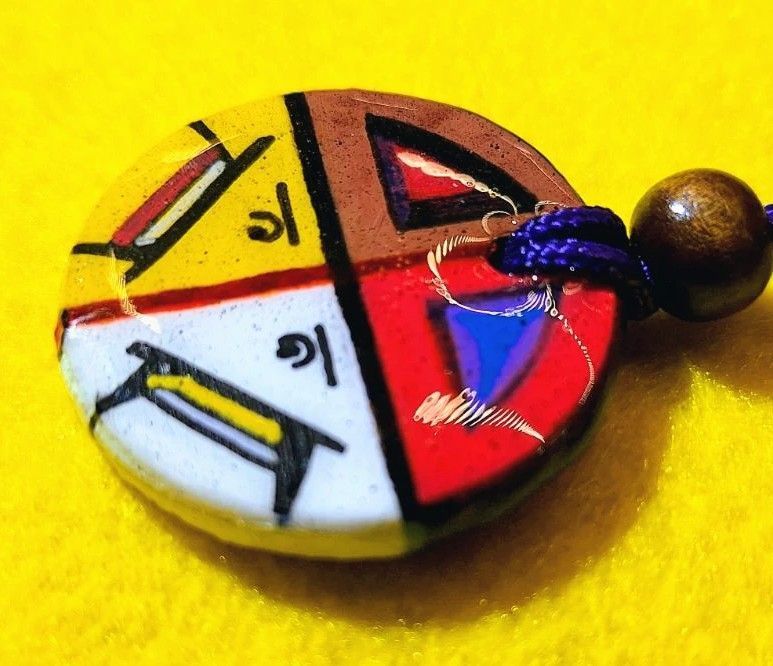 Colorful circular pendant, divided into four sections with symbols and Tibetan script.