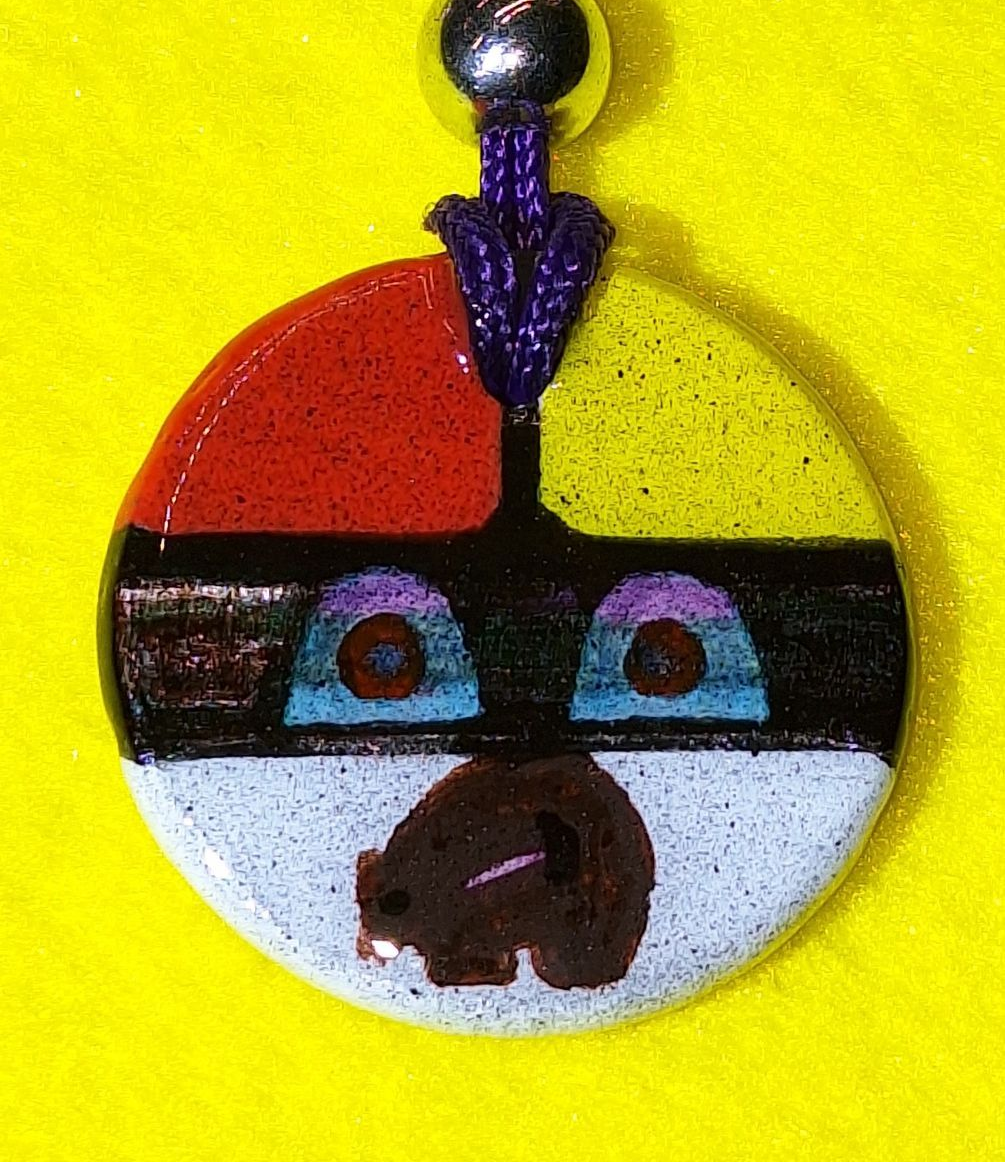 Colorful circular pendant with abstract face design; red, yellow, black, and white sections.