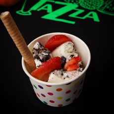 A cup of ice cream with strawberries and a waffle stick