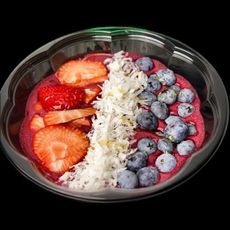 A bowl of smoothie with strawberries , blueberries and coconut on a black background.