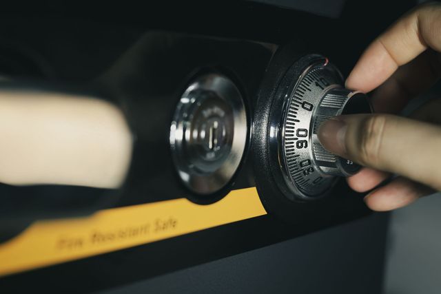 A hand turns a combination dial on a black safe or lockbox