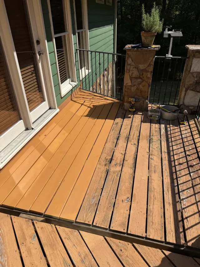 Weathered wooden porch deck with sunlit railings and a small stone post