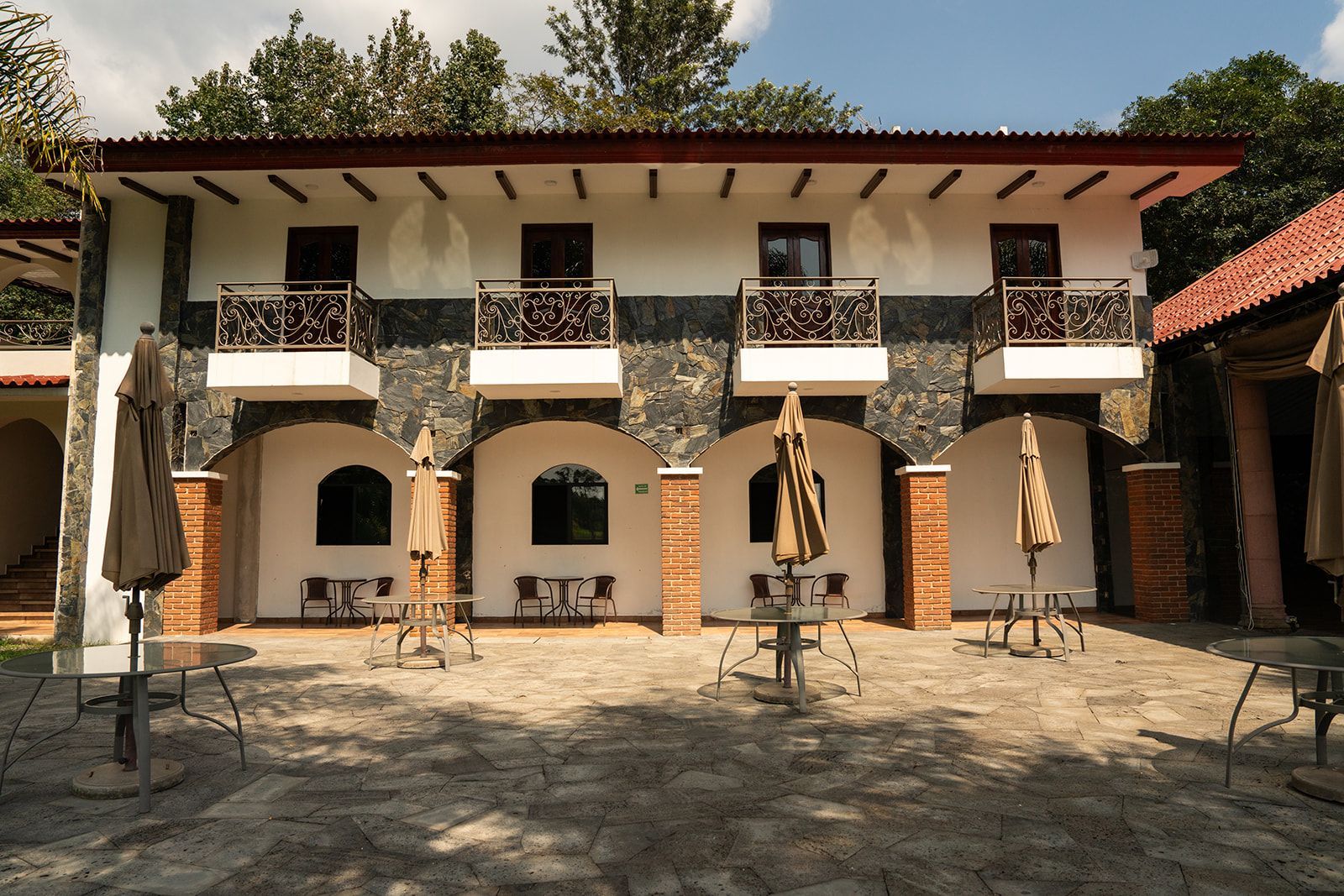 Courtyard of a two-story white building with arches, balconies, and closed umbrellas under a blue sky