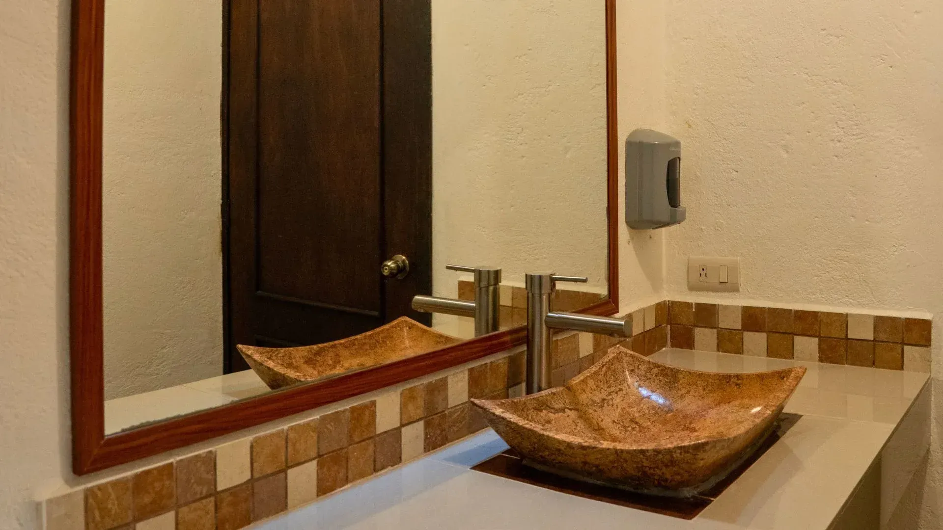 Mueble de baño con lavabo de piedra, espejo y paredes y encimera de azulejos beige.