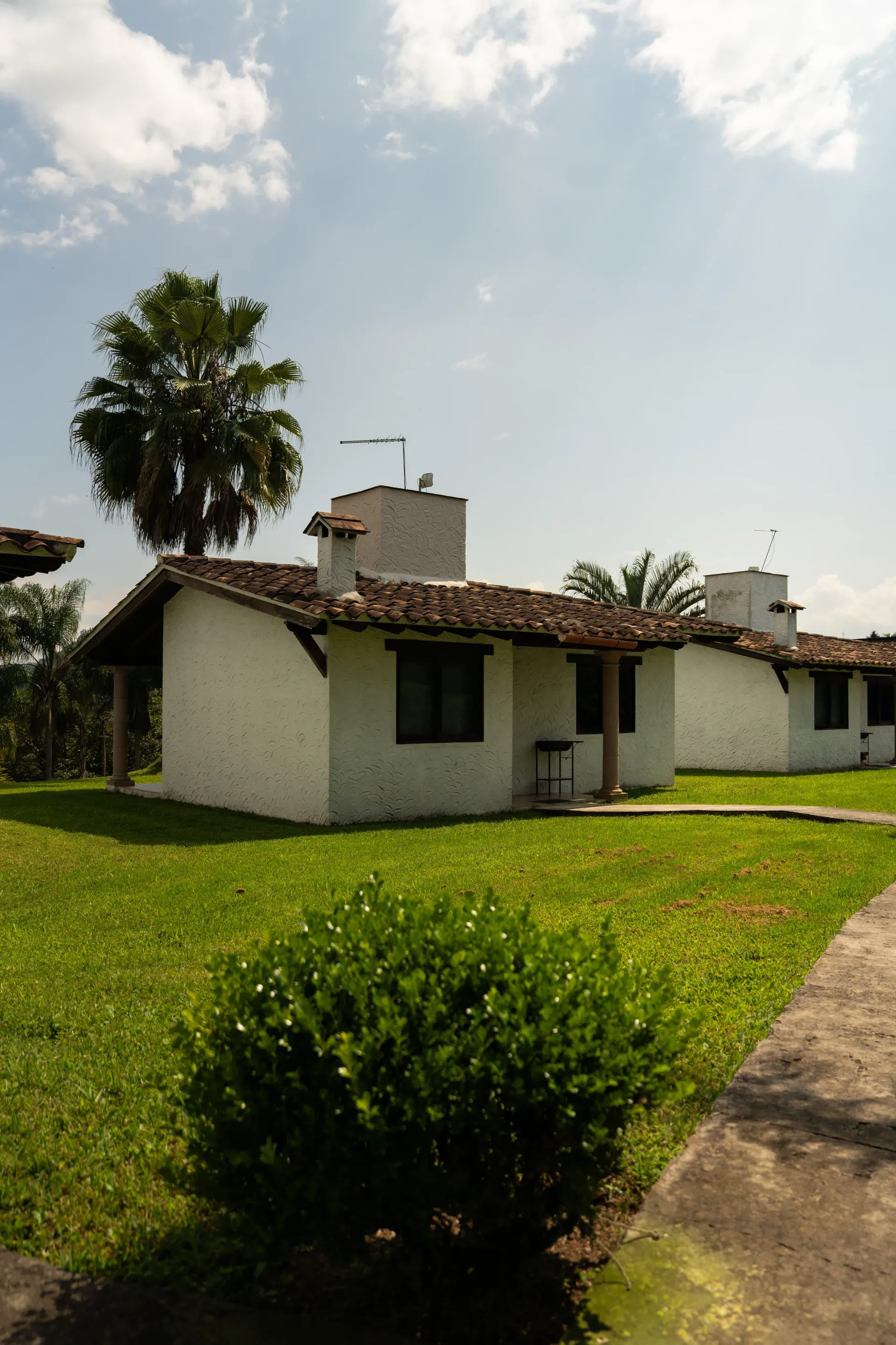 Pequeña casa blanca con tejado de tejas y césped verde bajo un cielo brillante.