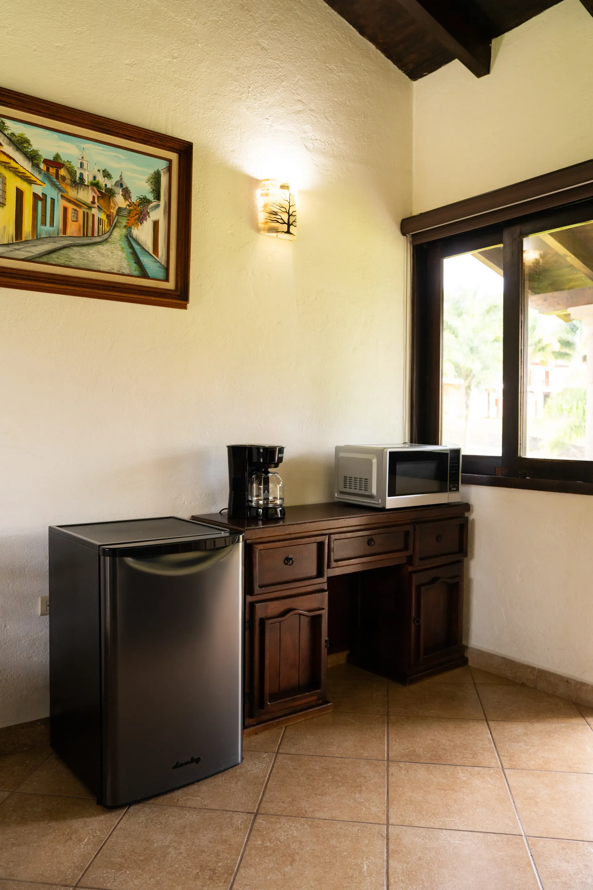 Small room with mini fridge, coffee maker, microwave, and wooden desk by a window