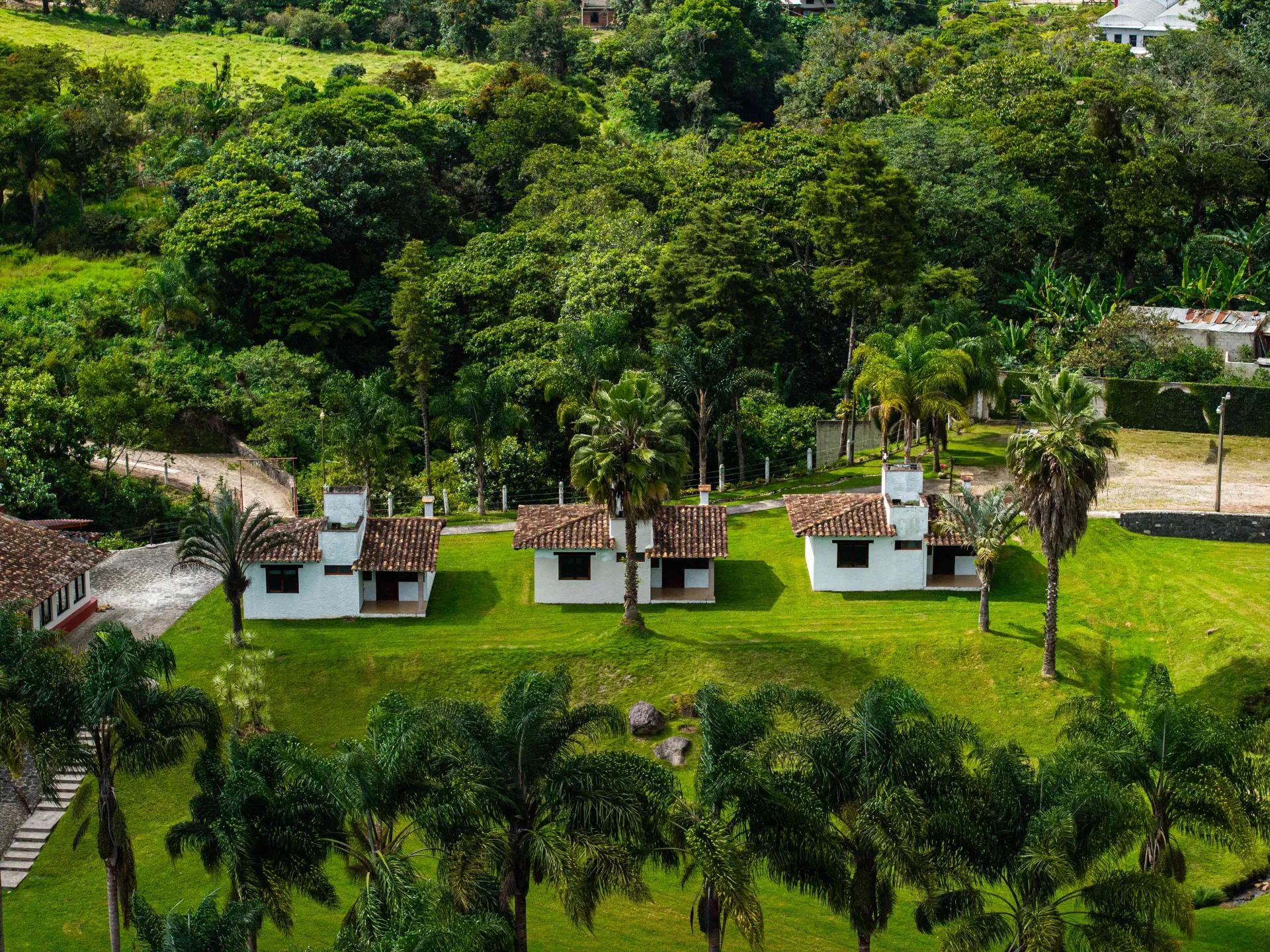 Green garden with three white cabanas under trees and a lush hillside backdrop
